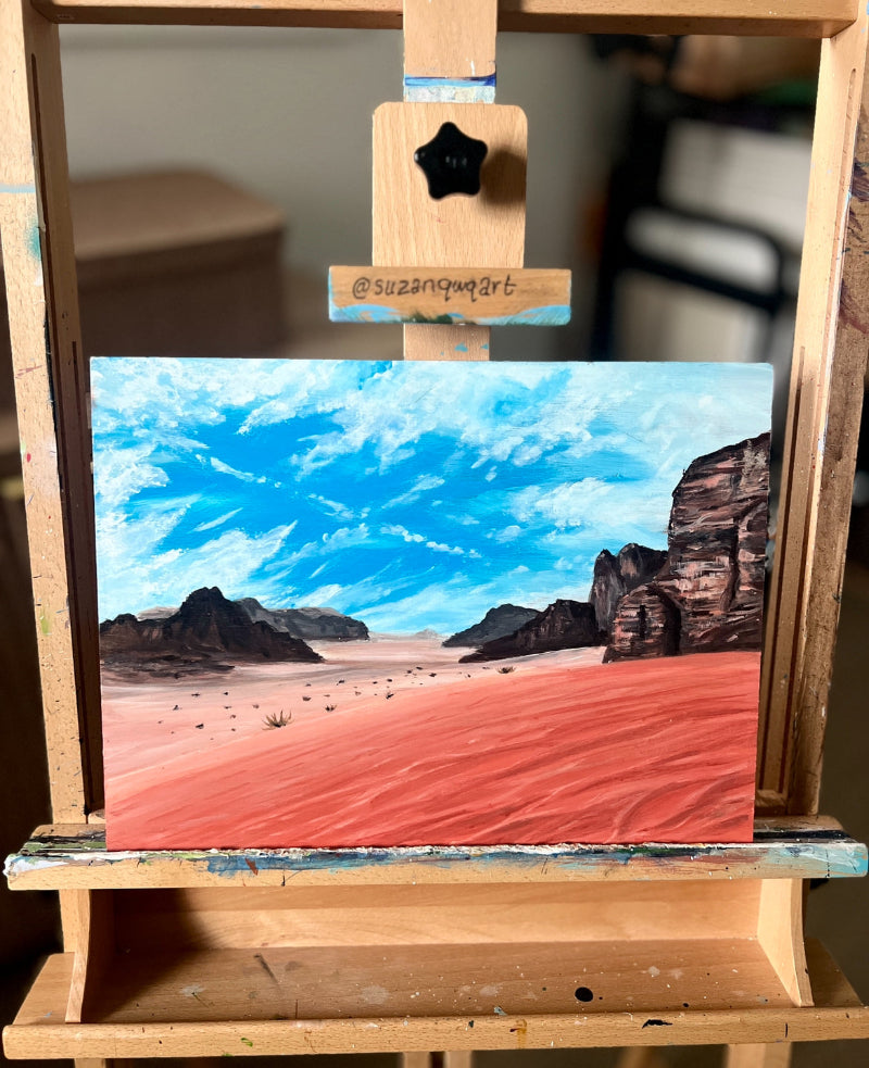 Painting of a desert landscape on a wooden easel with 'suzannqart' signature.